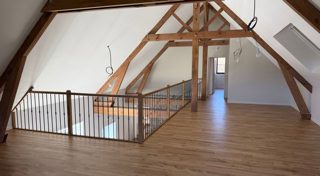Aménagement intérieur avec charpente bois apparente, parquet et garde-corps réalisé par Graille Menuiserie.