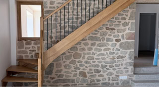 Escalier sur mesure en bois avec garde-corps métallique, intégré dans un intérieur avec mur en pierre.